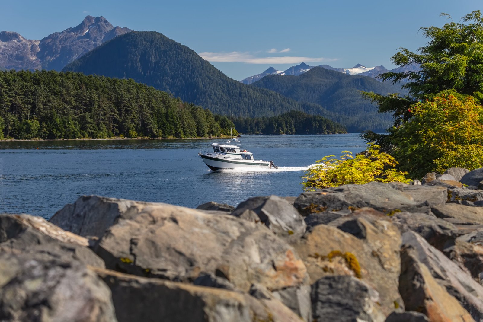 Fishing speedboat sailing fast in harbor. Beautiful yellow trees and rocks in soft focus in the foreground. Mountains, and forest in the background.
